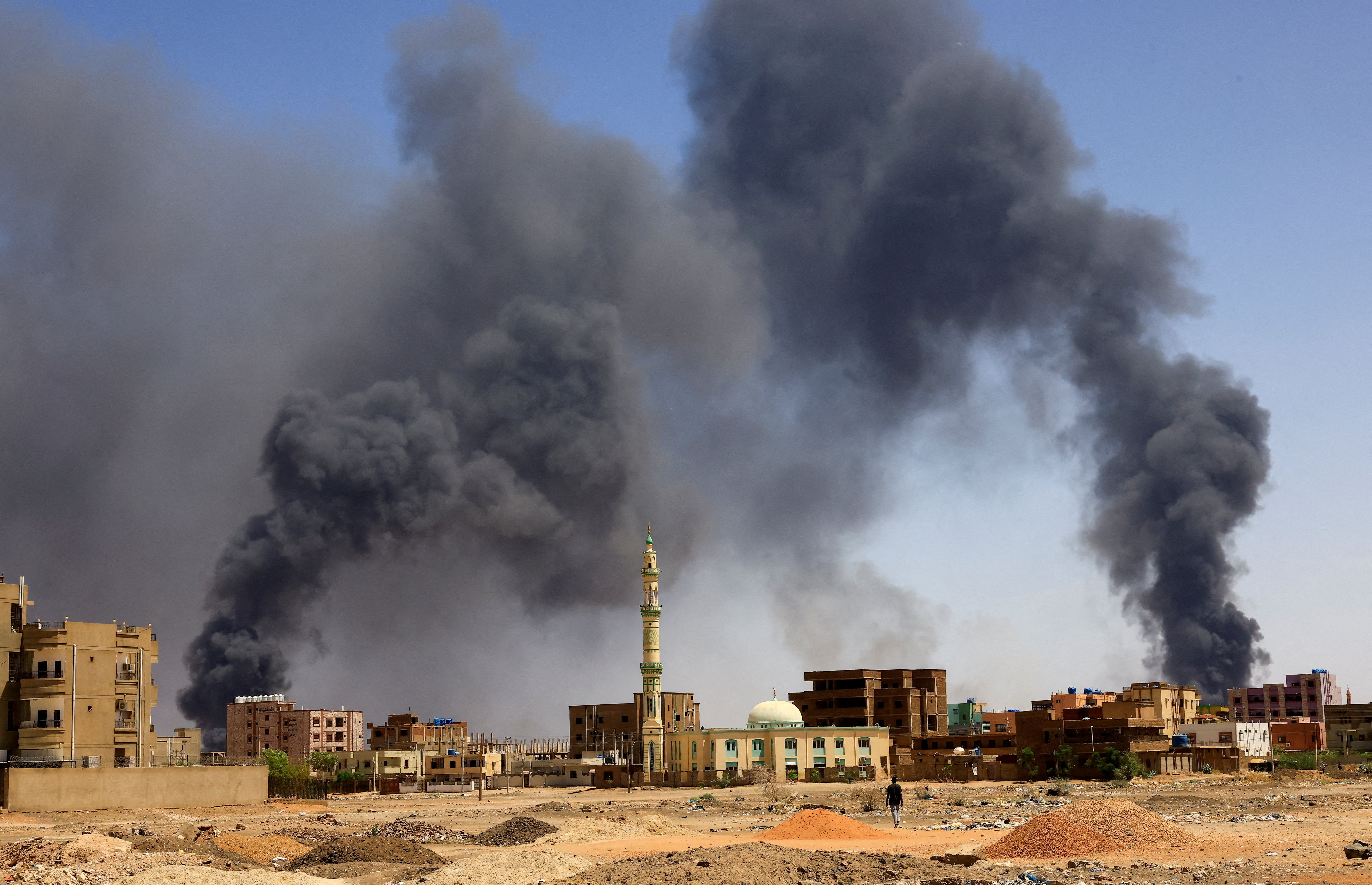 A man walks while smoke rises above buildings after aerial bombardment