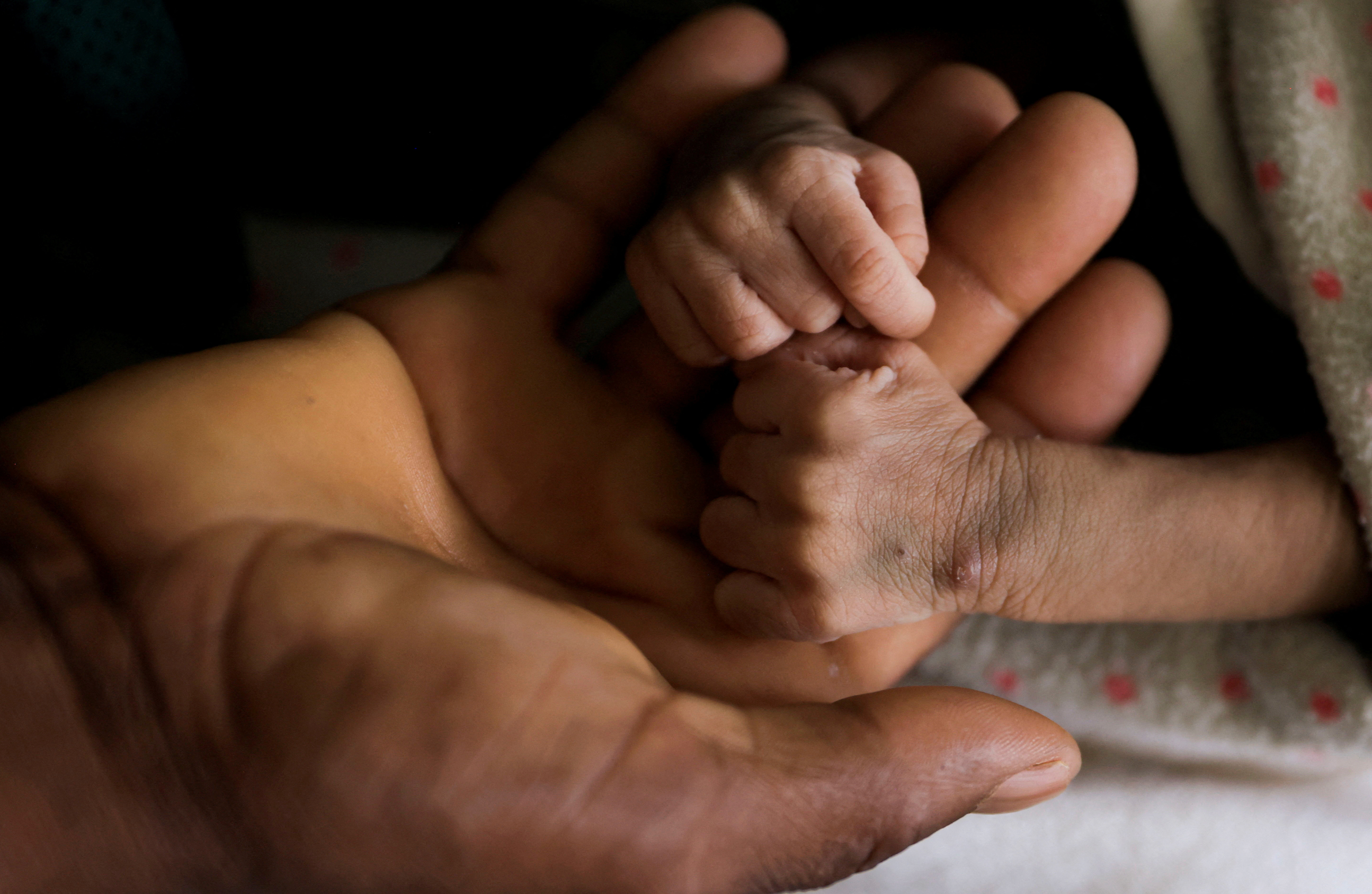Woldegebrial Abadi, 36, holds the hands of his severely malnourished newborn son