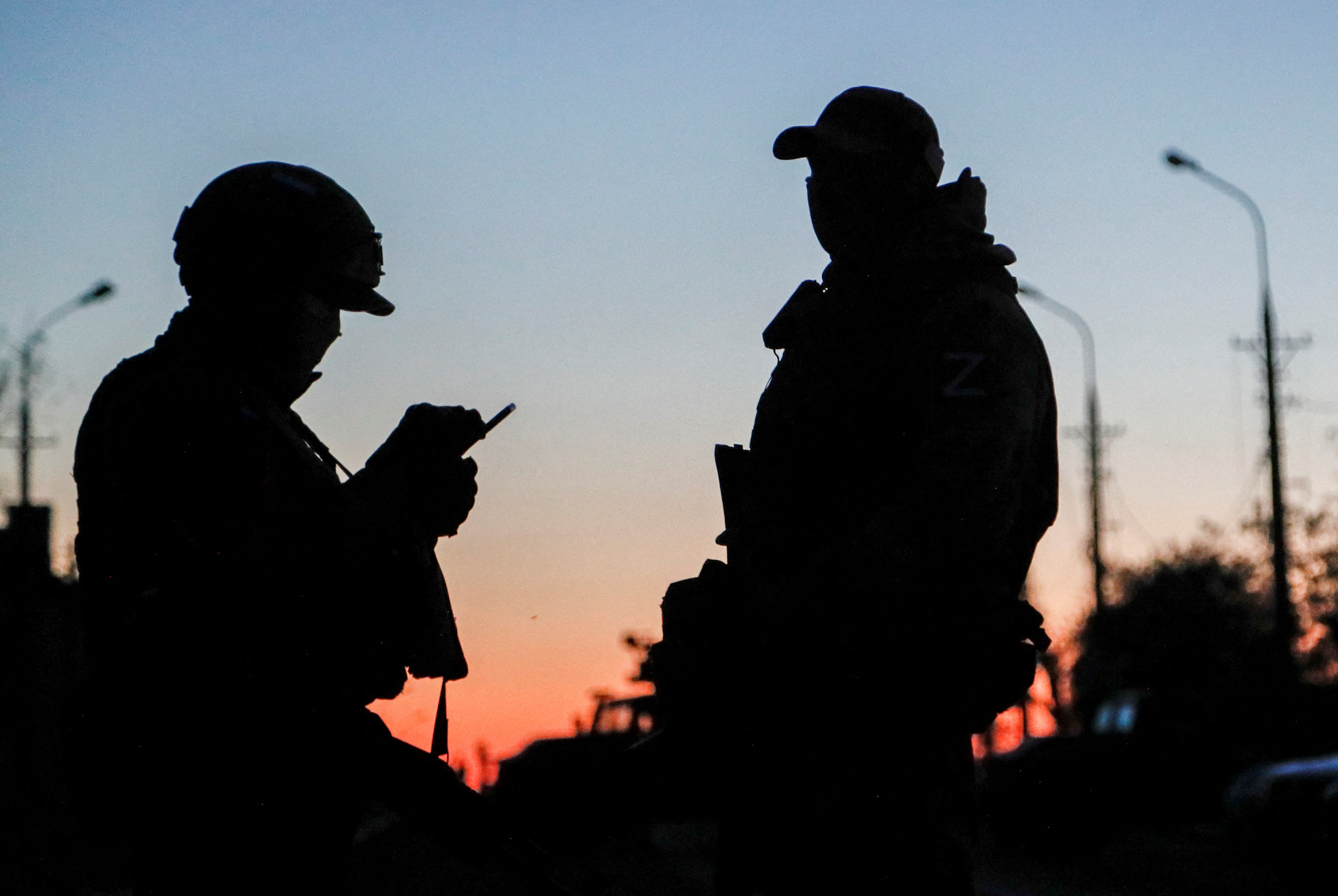 Russian service members stand guard on a road during sunset before the expected evacuation of wounded Ukrainian soldiers from the besieged Azovstal steel mill