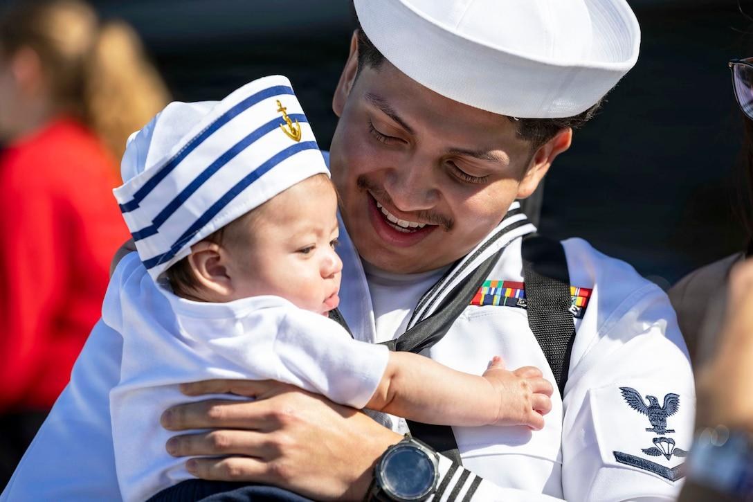 Navy Petty Officer 3rd Class Omar Mora meets his newborn child for the first time at Naval Station Norfolk, Virginia, on May 16, 2026, following an 11-month deployment aboard USS Gerald R. Ford. Navy leaders now say sailors assigned to deploying carrier
