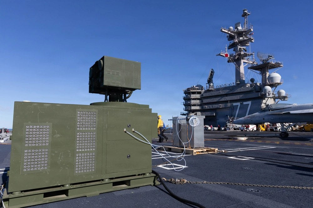 A containerized LOCUST Laser Weapon System sits on the flight deck of the aircraft carrier USS George H.W. Bush during Navy live-fire testing in the Atlantic Ocean, Oct. 6, 2025. The system detected, tracked, engaged and neutralized multiple unmanned