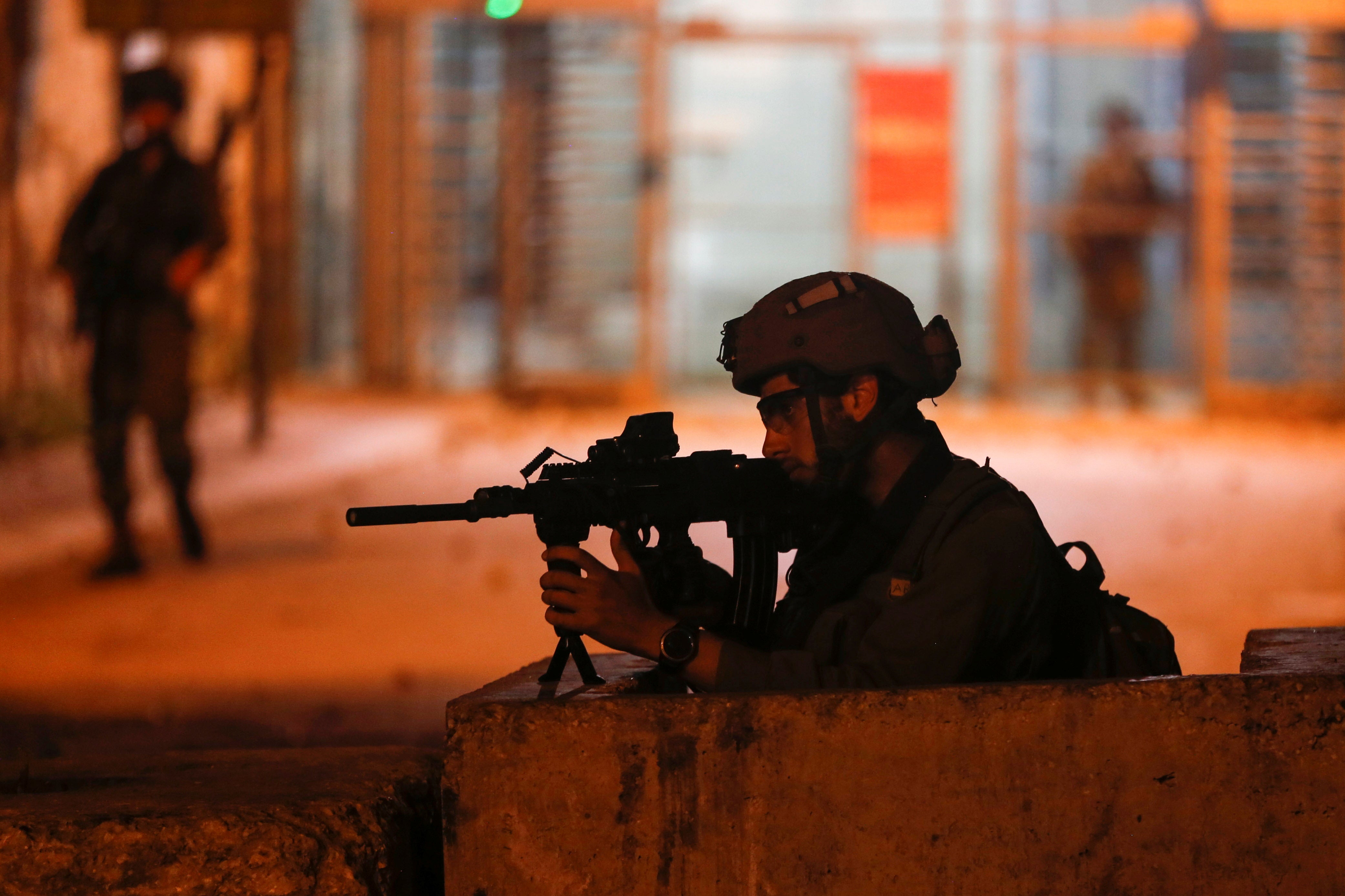 member of Israeli forces aims his weapon as Palestinians take part in an anti-Israel protest over tension in Jerusalem, in Hebron in the Israeli-occupied West Bank