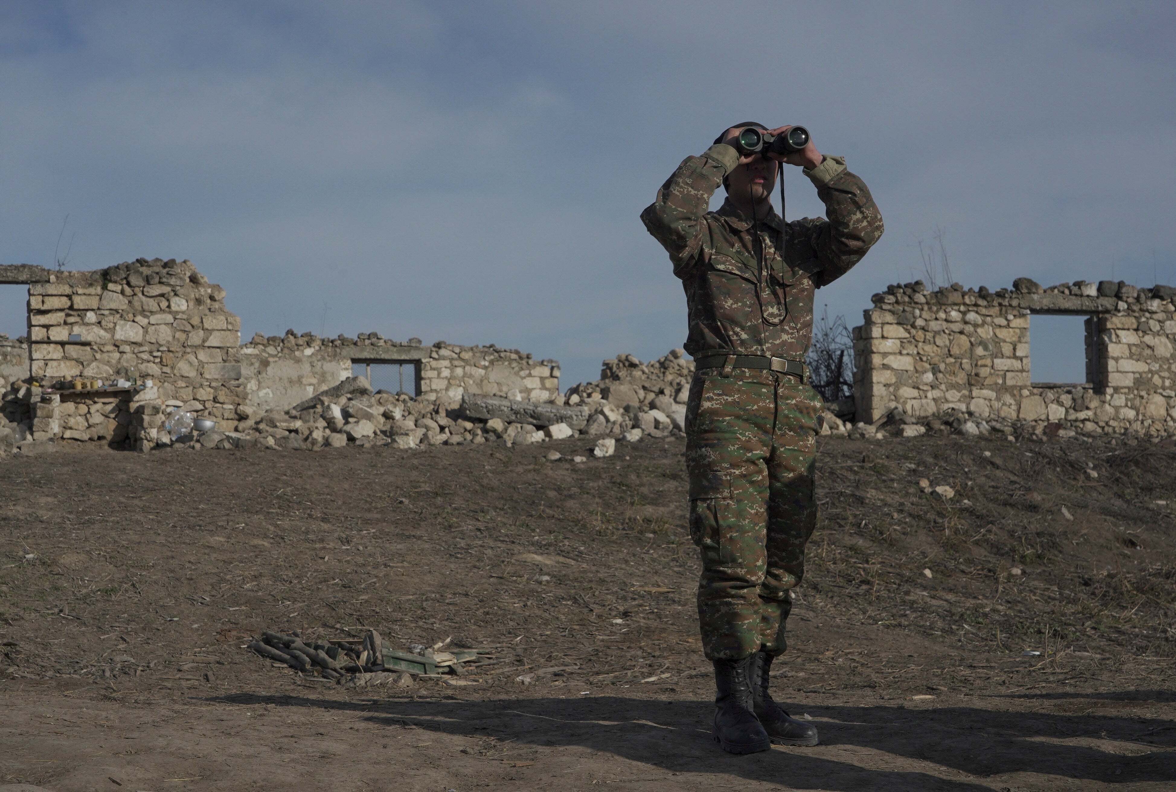 An ethnic Armenian soldier looks through binoculars as he stands at fighting positions near the village of Taghavard in the region of Nagorno-Karabakh