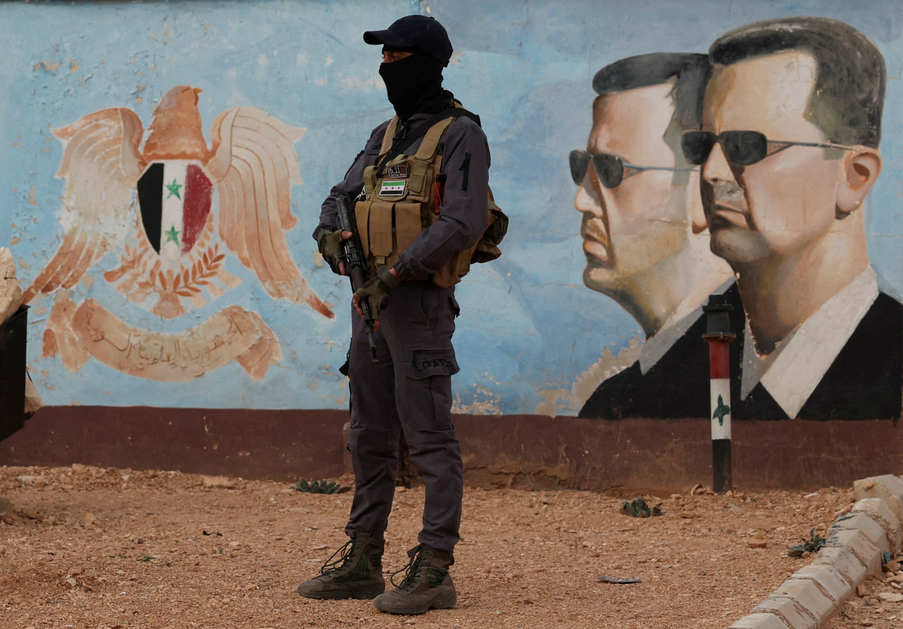FILE PHOTO: A member of the former rebel group Hayat Tahrir al-Sham stands guard near an image of Syria's Bashar al-Assad at the fourth division headquarters in Damascus, Syria, January 23, 2025 REUTERS/Yamam Al Shaar/File Photo