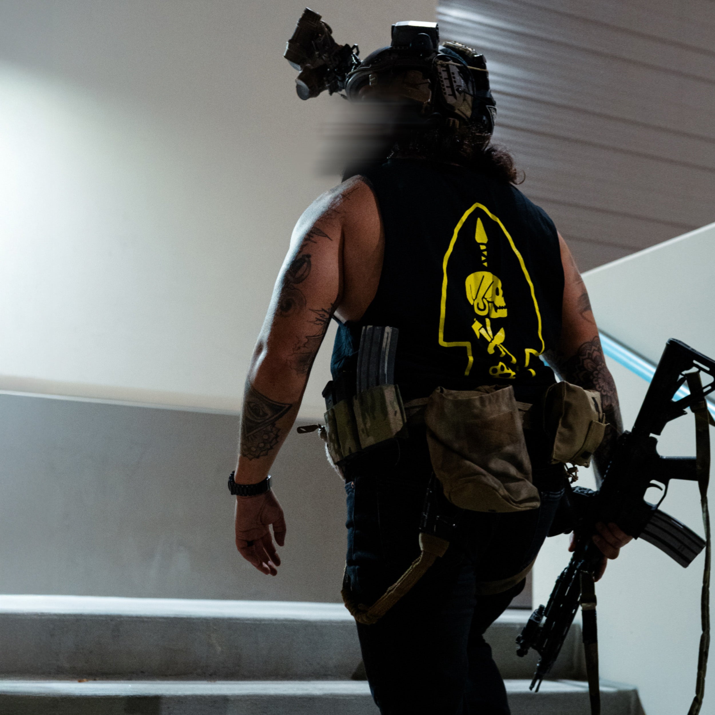 Person wearing tactical gear with a yellow logo on a neutral background