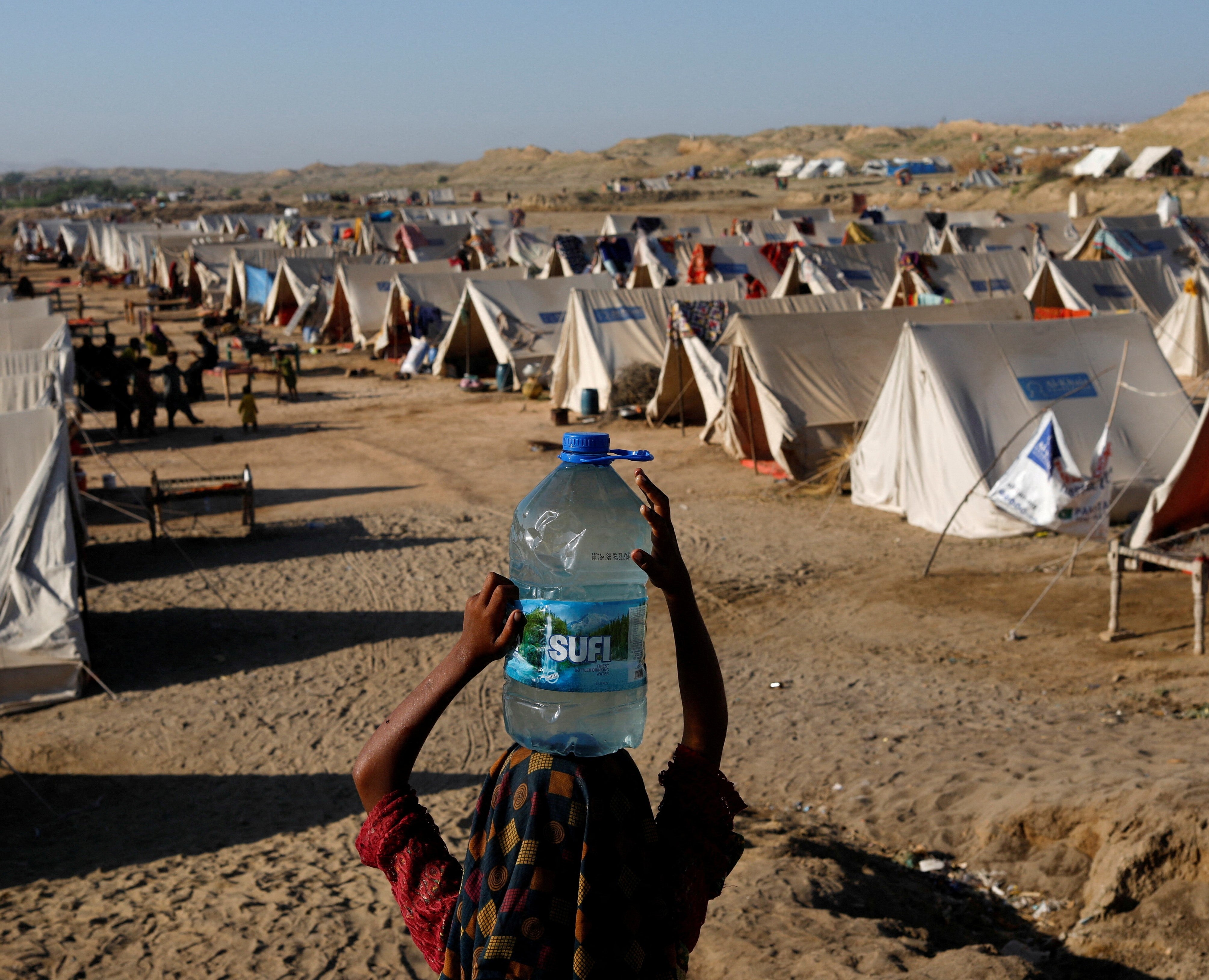 A displaced girl carries a bottle of water she filled from nearby stranded flood-waters