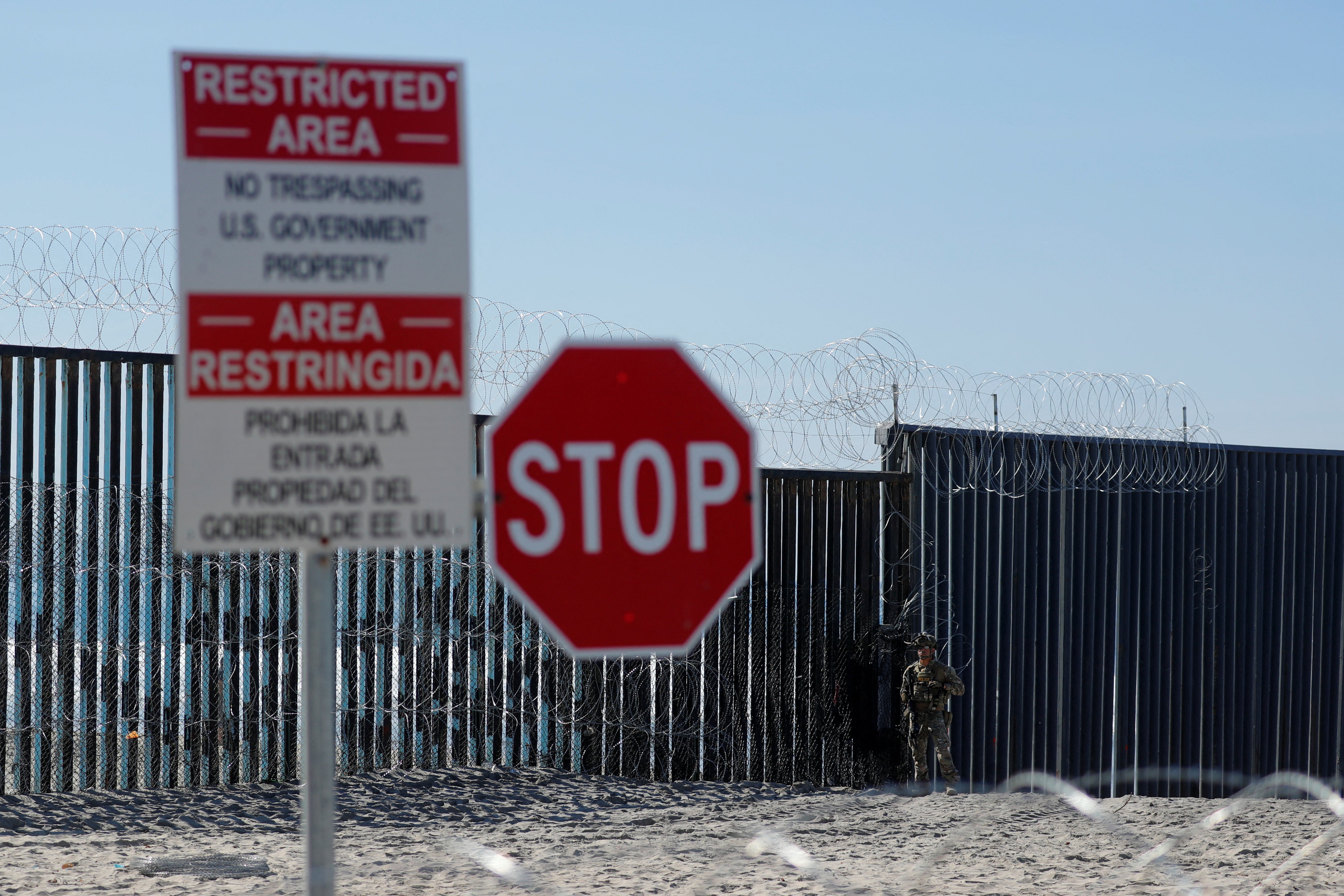 An armed U.S. Customs and Border Patrol agent stands watch at the border fence