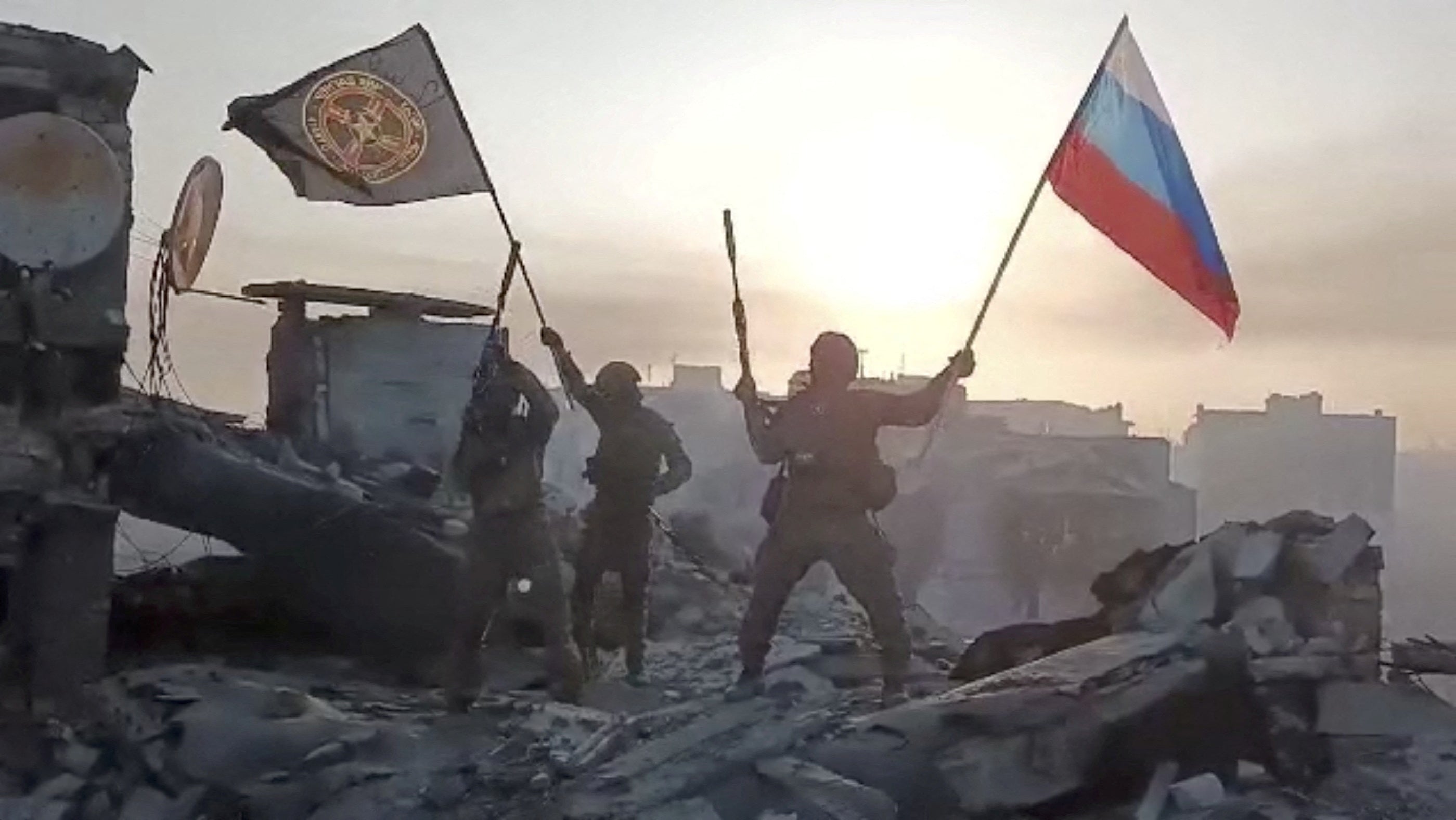 Wagner mercenary group fighters wave flags of Russia and Wagner group on top of a building in an unidentified location, in the course of the Russia-Ukraine conflict