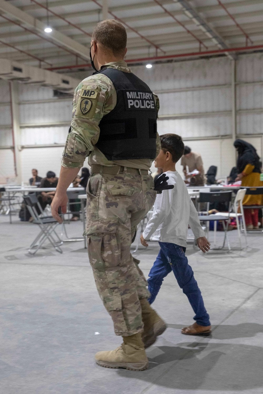 Illustrative file photo — A U.S. Army military police officer walks with an Afghan evacuee child at Camp As Sayliyah, Qatar, Aug. 26, 2021. U.S. Army photo by Spc. Elizabeth Hackbarth