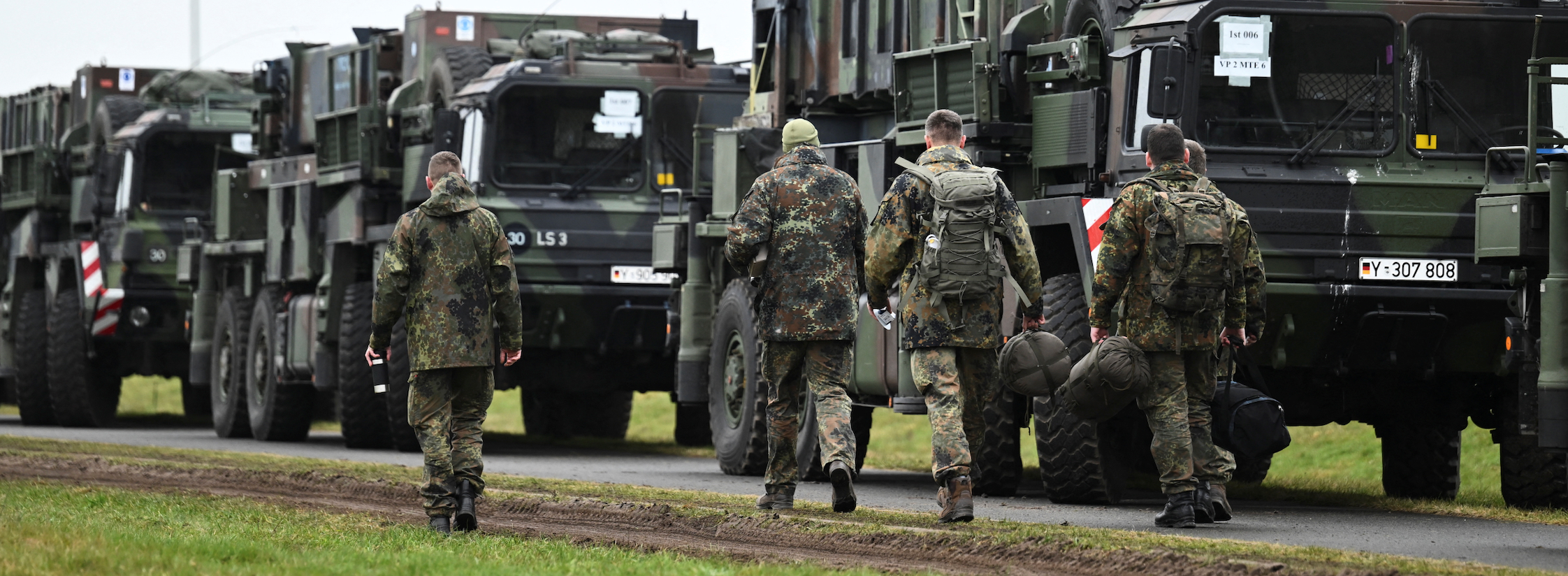 German Air Force soldiers walk past convoy vehicles, as Patriot mobile defense surface-to-air missile systems are transported to Poland