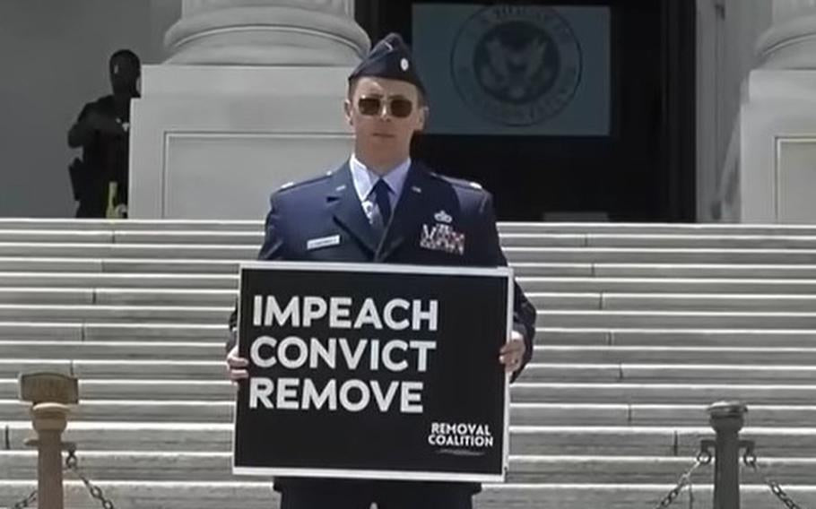 Air Force Maj. Jason Watson stands on the U.S. Capitol steps holding a sign calling for the impeachment, conviction and removal of President Donald Trump and Vice President JD Vance on July 1, 2026. His attorney said October 9 that Watson remains in
