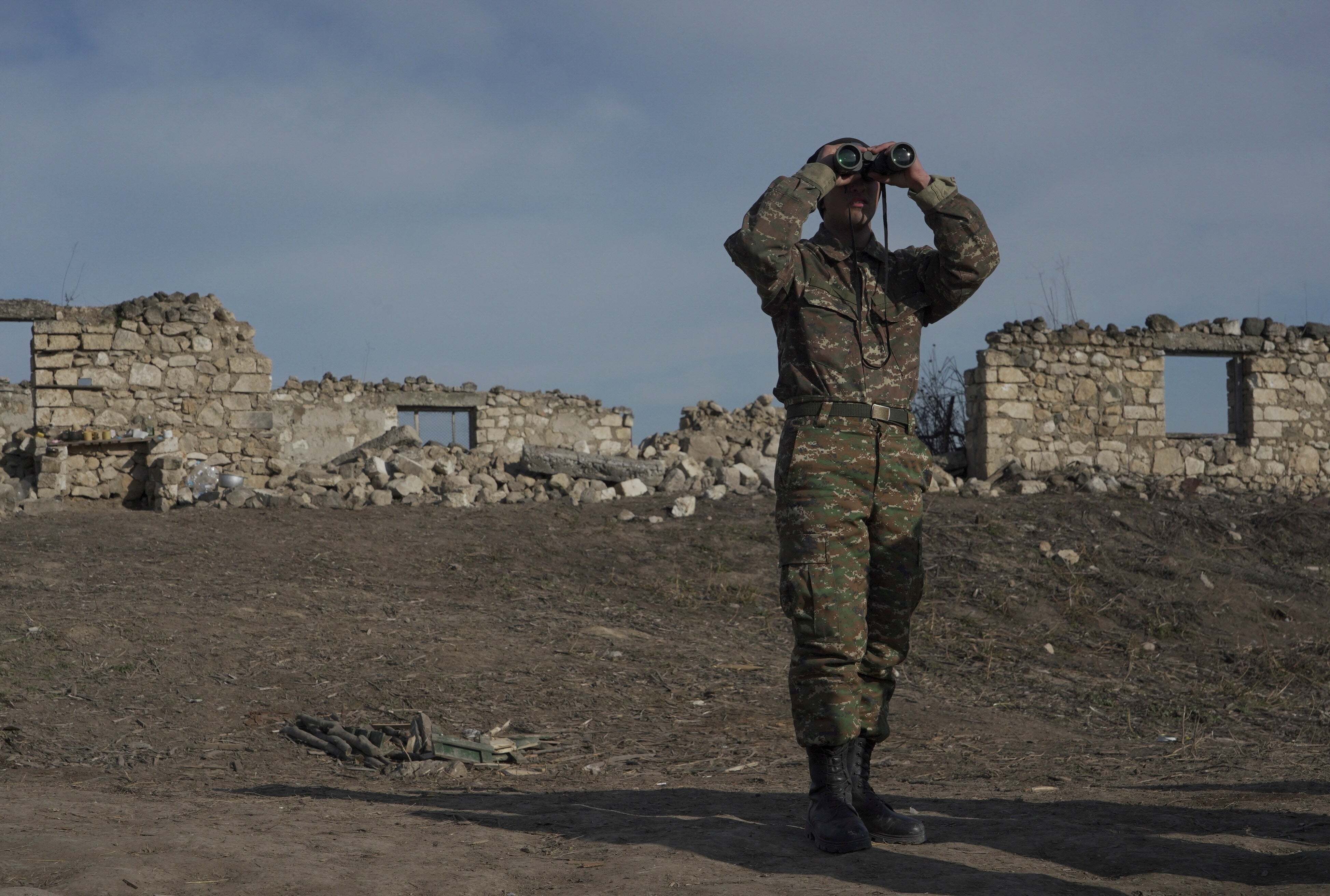  An ethnic Armenian soldier looks through binoculars as he stands at fighting positions near the village of Taghavard in the region of Nagorno-Karabakh